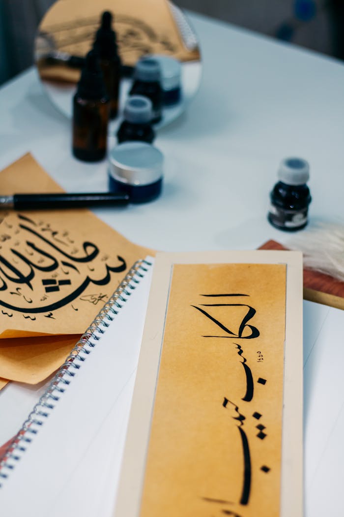 gallery-5 Close-up of Arabic calligraphy art with ink bottles and brush on a desk.
